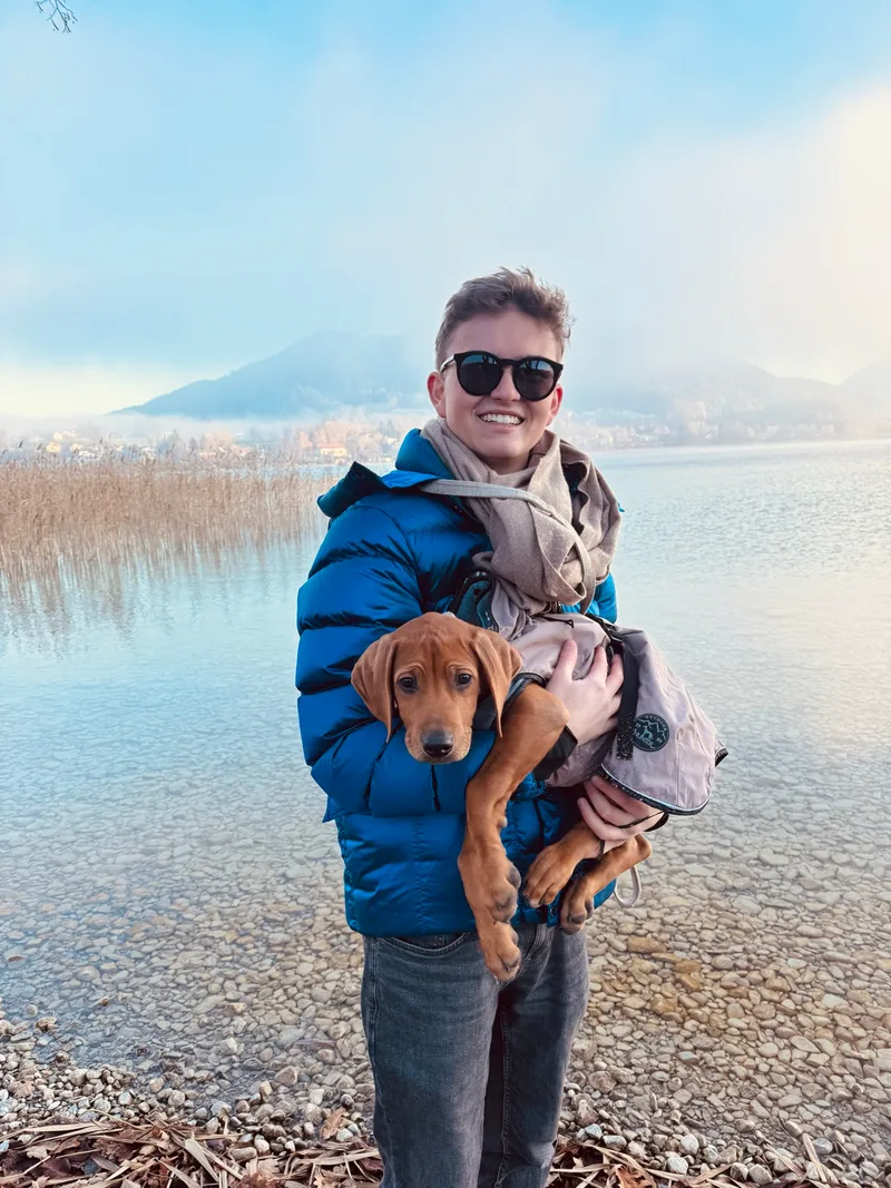 Luis Tillman mit einem Hundewelpen auf dem Arm am Seeufer
