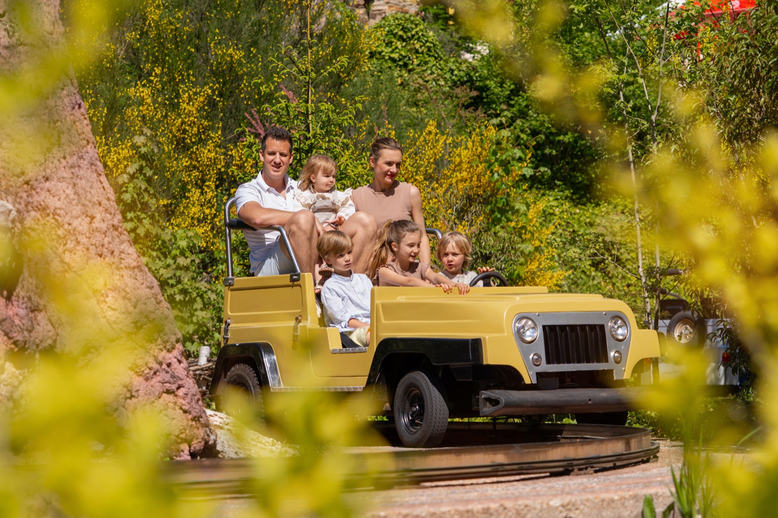 Familie im gelben Jeep-Fahrgeschäft zwischen blühenden Sträuchern im Taunus Wunderland
